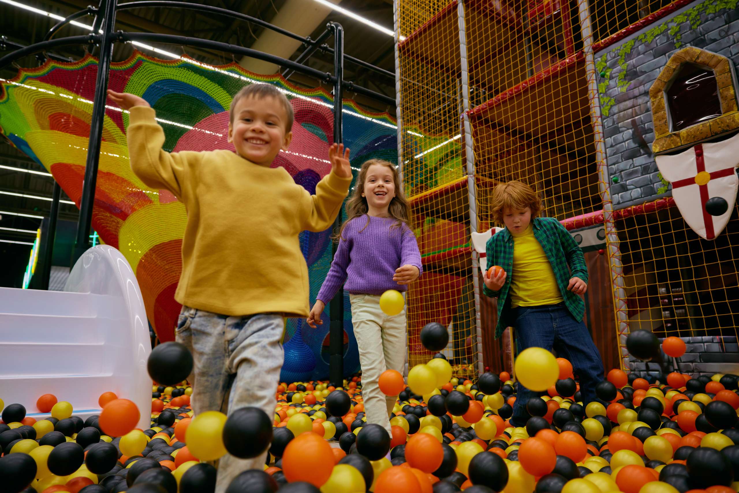 Cheerful little children spending time at daycare indoor playground. Game center for kids excited recreation time. Portrait of boys and girl playing in colorful ball pit